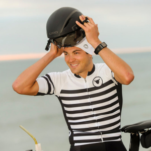 Man wearing a black Chrome Dome Cap on a bicycle holding helmet and sunglasses.